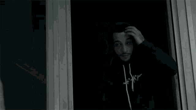 a man wearing a black hoodie with the word house on it looks out a window