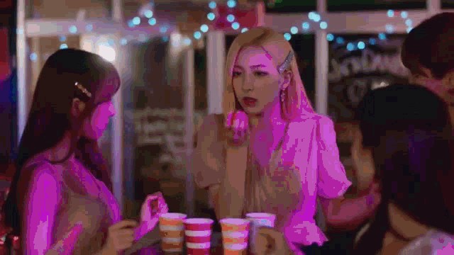 a group of young women are standing around a table holding cups of coffee .