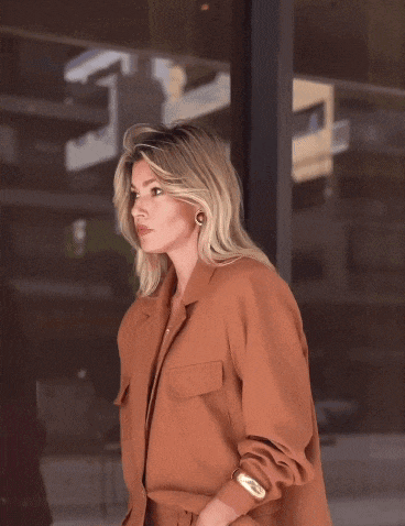 a woman wearing a brown jacket and pants is standing in front of a building