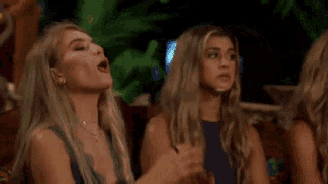 two women are sitting next to each other on a couch and praying with their hands in the air .