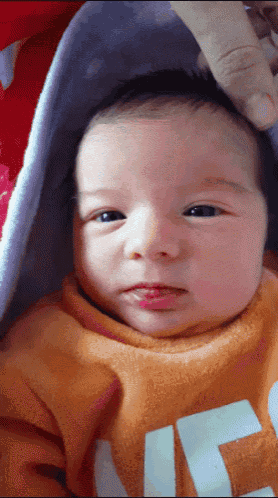 a baby is wearing an orange sweater with the letter g on it