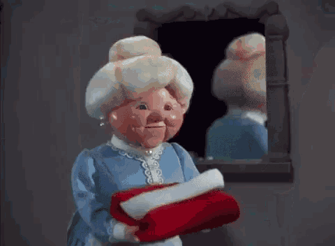 a doll in a blue dress is holding a red blanket in front of a mirror .