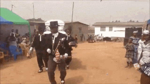 a man in a top hat is carrying a coffin down a dirt road
