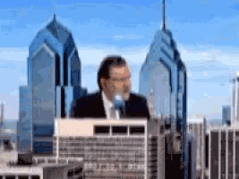 a man in a suit and tie is standing in front of a microphone in front of a city skyline