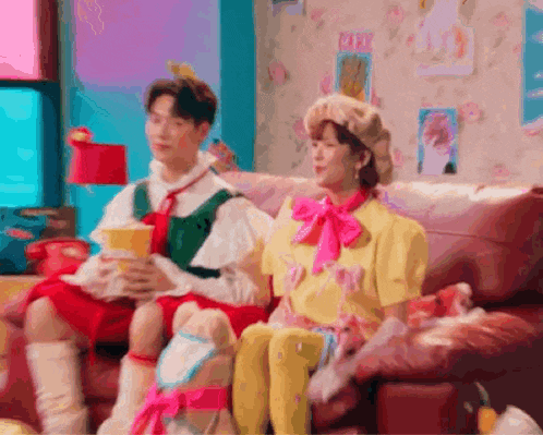 a man and a woman are sitting on a couch . the woman is wearing a pink bow tie .