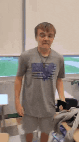 a young man wearing a gray shirt with an american flag on it is standing in a room .