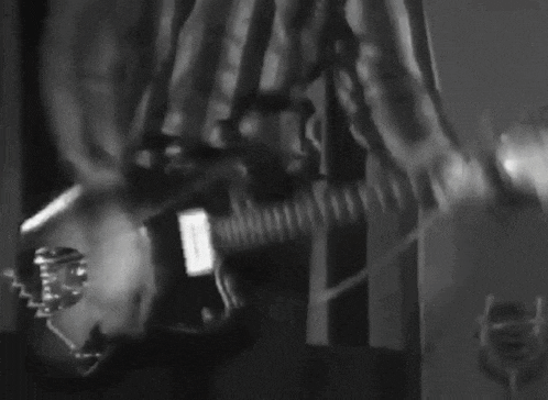 a black and white photo of a woman singing into a microphone in front of a crowd .