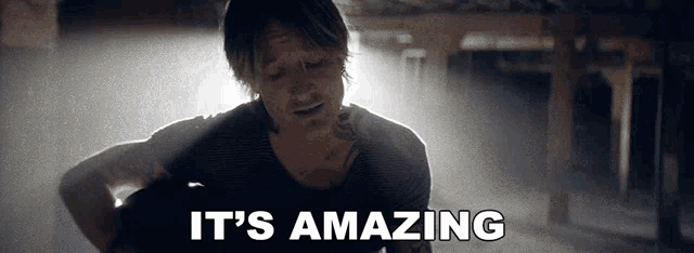 a man with a tattoo on his chest is holding a guitar and says it 's amazing