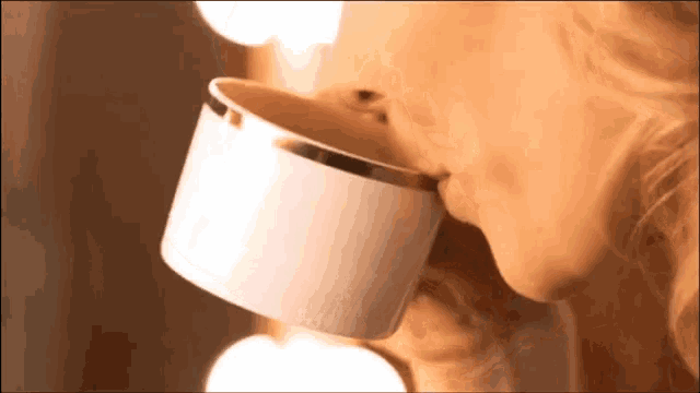 a woman is drinking from a white cup with gold trim