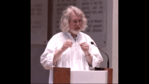 a man with long hair and a beard stands at a podium