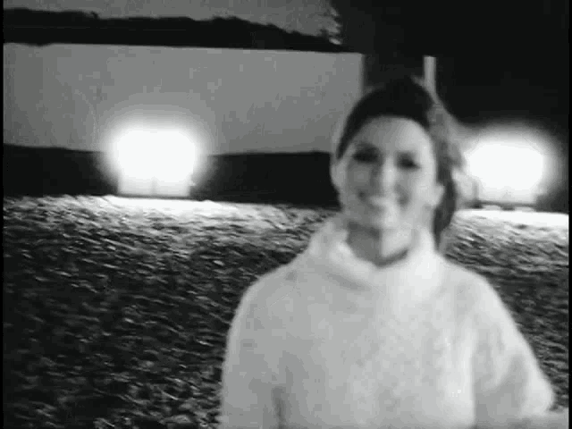 a black and white photo of a woman in a white sweater standing in a field .
