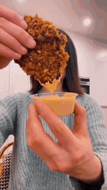 a woman is dipping a piece of food into a small container of sauce