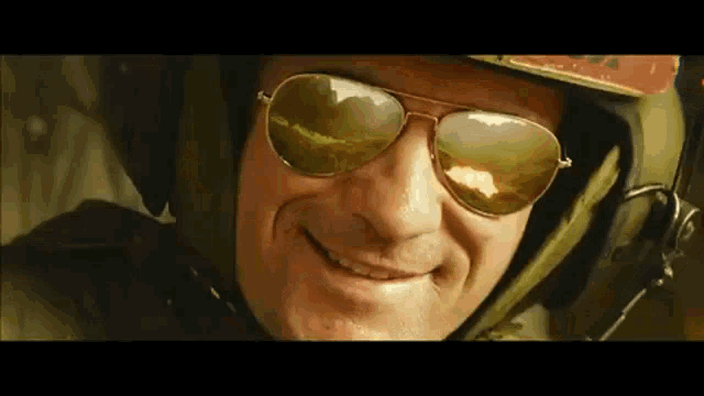 a man wearing a helmet and sunglasses smiles for the camera