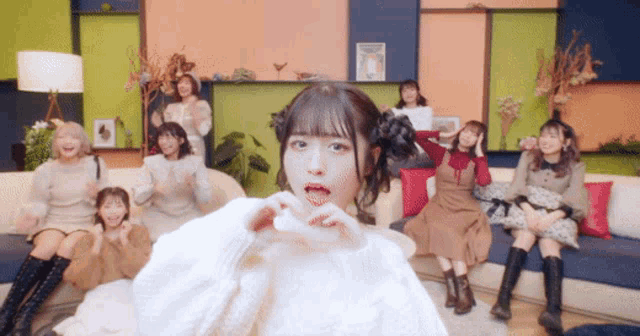 a group of girls are sitting on a couch with one girl making a heart with her hands