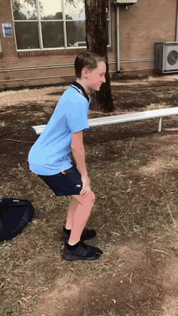 a boy in a blue shirt and black shorts squatting on the grass