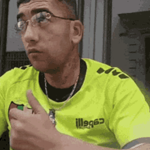 a man wearing glasses and a neon yellow shirt giving a thumbs up .