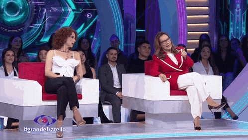 two women are sitting on a stage with a sign that says grande