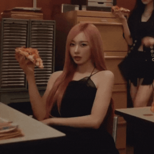 a woman in a black dress holds a slice of pizza in her hand