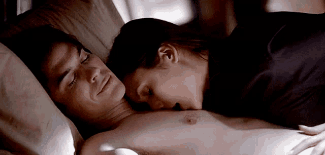 a woman kisses a man 's chest while laying in bed