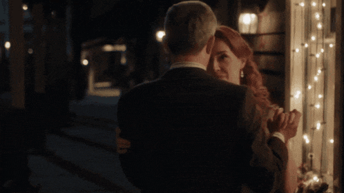 a man and woman dancing in front of a window with lights