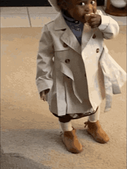a little girl wearing a white trench coat and brown shoes