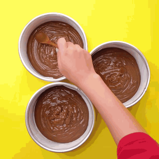 a person is mixing a chocolate cake batter in three pans