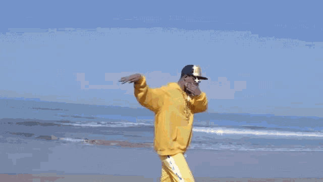 a man wearing a yellow hoodie and a hat is dancing on the beach .