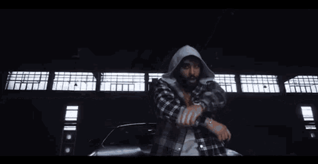 a man wearing a plaid shirt and a hood is standing in front of a building .