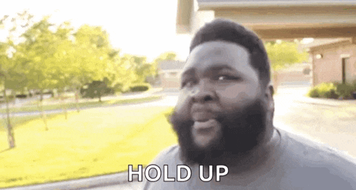 a man with a beard is standing in front of a house and talking .