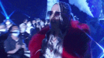 a woman wearing sunglasses and a red fur coat is standing in front of a crowd of people .