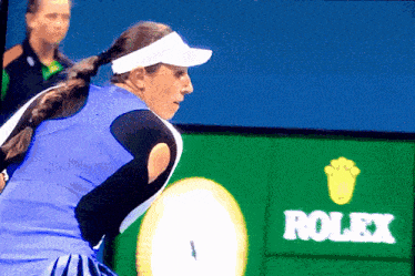 a tennis player stands in front of a rolex advertisement