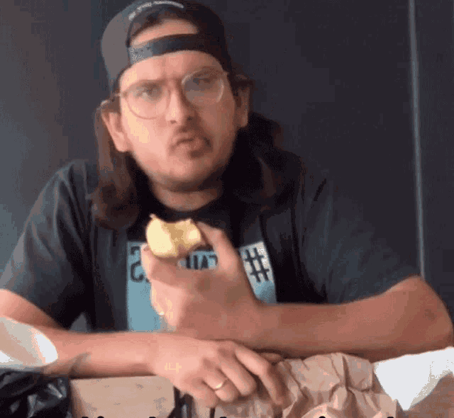 a man wearing glasses and a hat holds a piece of food