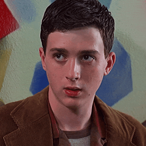a young man wearing a brown jacket and a striped shirt looks at the camera