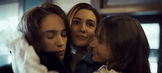 three women are hugging each other and one of them is kissing the other on the cheek