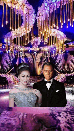 a man in a tuxedo and a woman in a dress are standing next to each other in front of a large chandelier