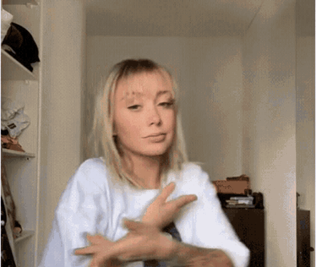 a woman with blonde hair and a tattoo on her arm is making a funny face with her hands .