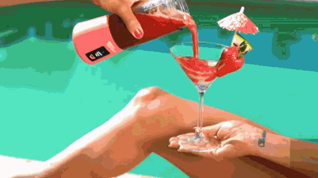 a person pouring a drink into a martini glass with an umbrella