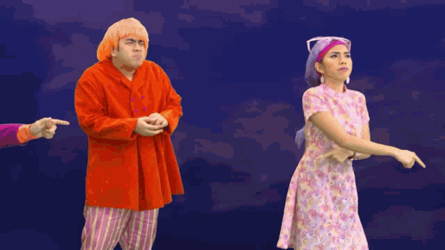 a man in an orange coat and a woman in a pink dress are pointing at each other