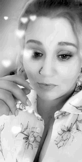 a woman with a nose ring is wearing a floral shirt and earrings .