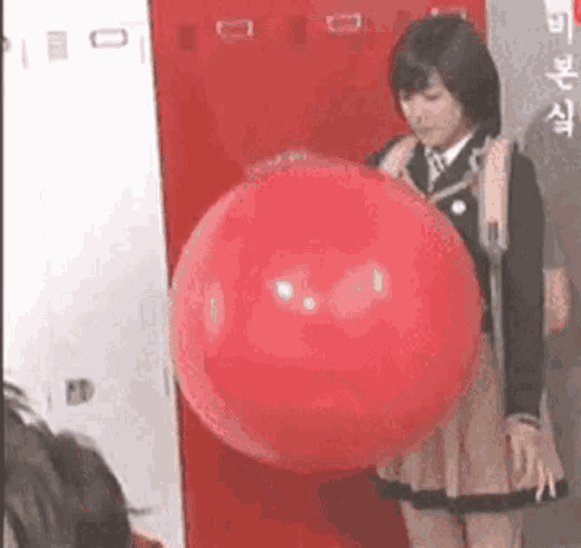 a woman in a school uniform is holding a large red balloon in her hand .
