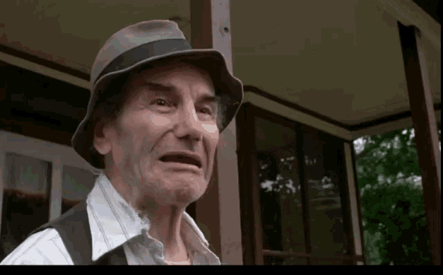 an older man wearing a hat and vest is making a face