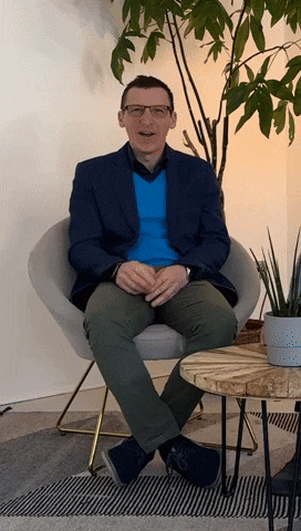 a man in a blue jacket sits in a chair in front of a plant