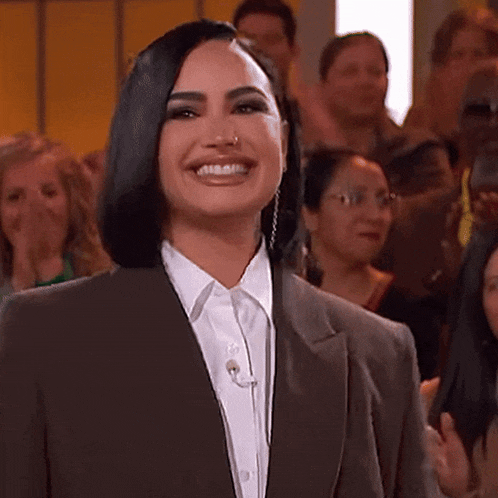 a woman in a suit and white shirt is smiling while standing in front of a crowd .