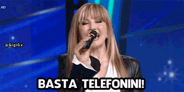 a woman singing into a microphone with the words basta telefonini on the bottom