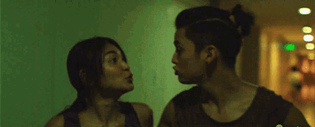 a man and a woman kissing in a hallway with a green exit sign in the background