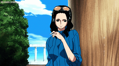 a woman in a blue shirt and sunglasses is standing in front of a wooden pillar and a balcony
