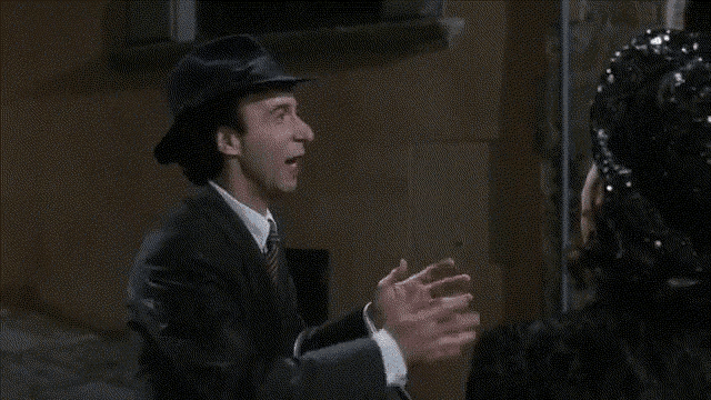 a woman in a black dress is talking to a man in a black hat with the words e questa written below her