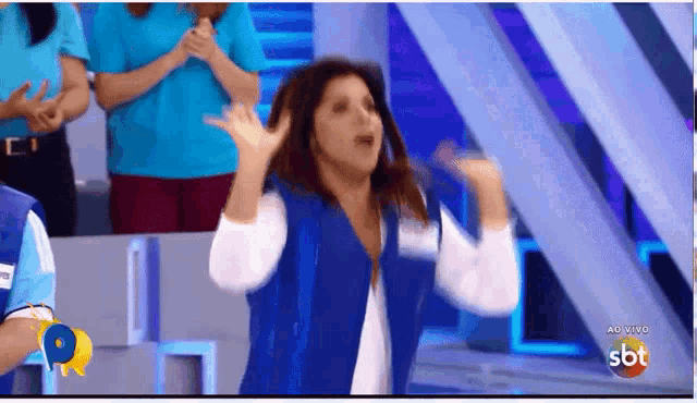 a woman in a blue vest is dancing in front of a crowd on a television screen that says sbt
