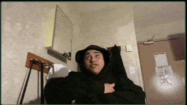 a man in a black hoodie is sitting on a bed