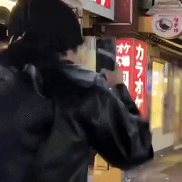 a person in a black jacket stands in front of a red sign that says karaoke